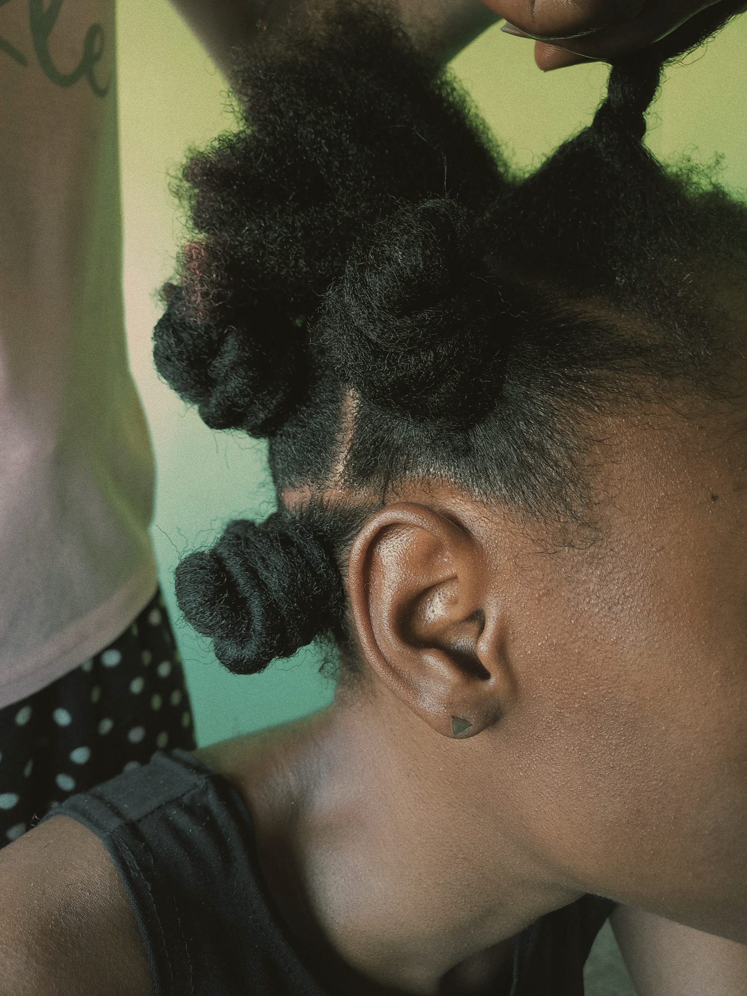 Natural hair being twisted into Bantu knots, close to the ear