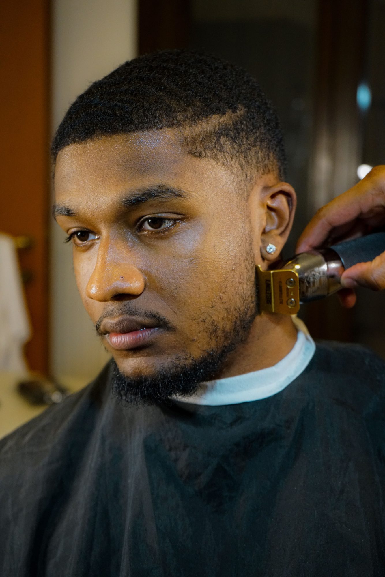 A barber lining up a short cut with clippers, the client in a black cape