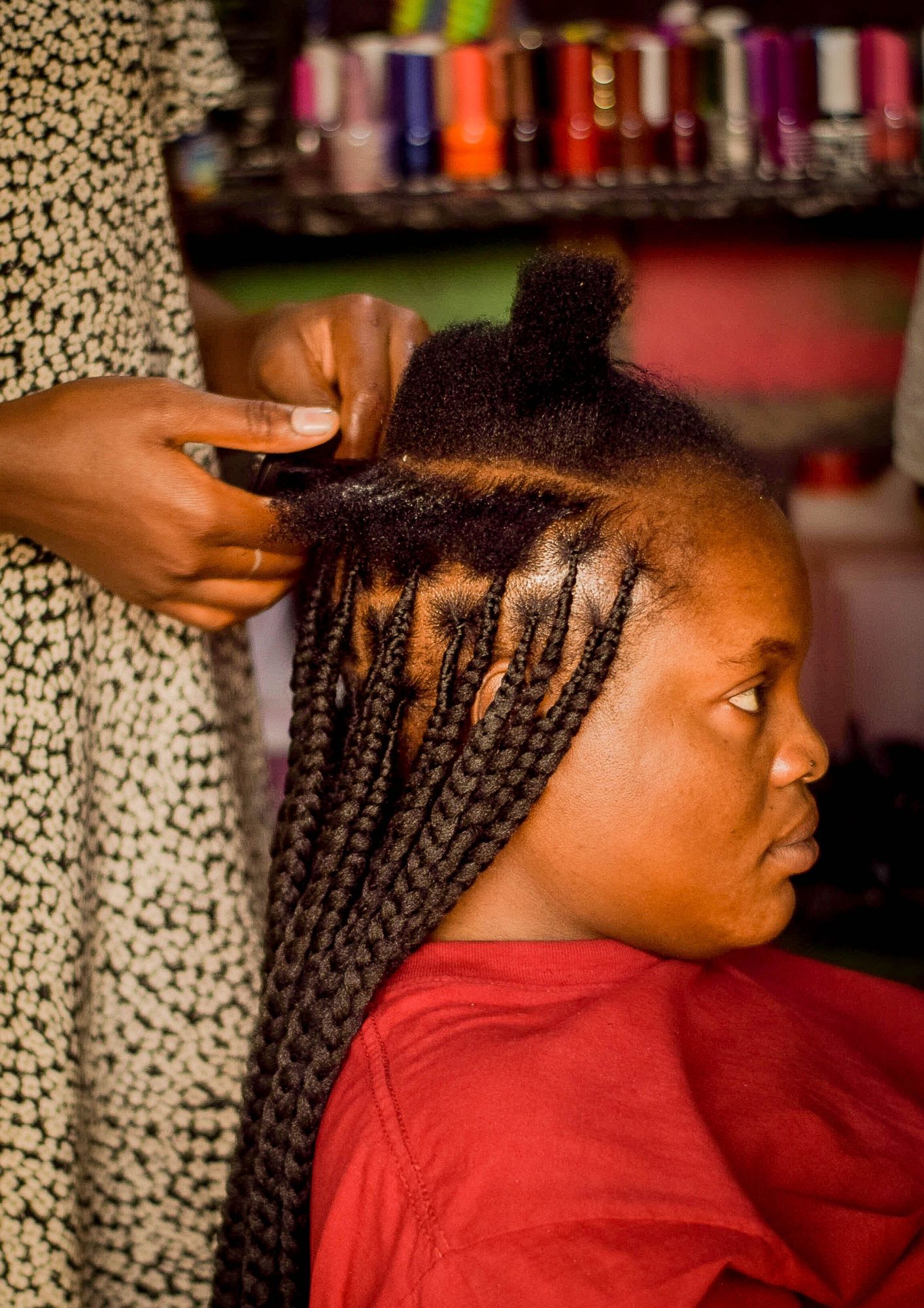 A stylist’s hands adding long box braids while a client sits in the chair