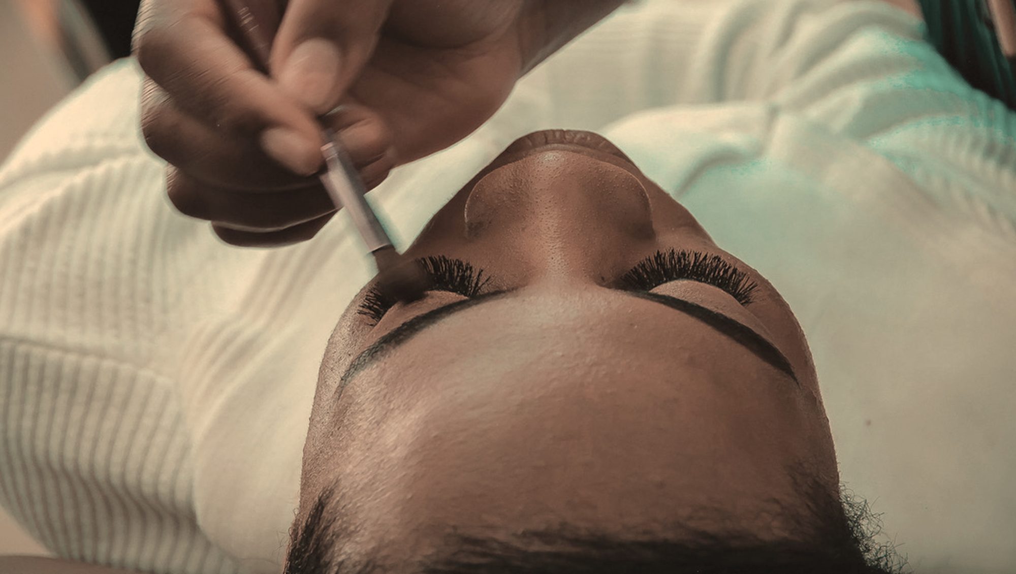 Lash extensions being placed with tweezers on closed eyes