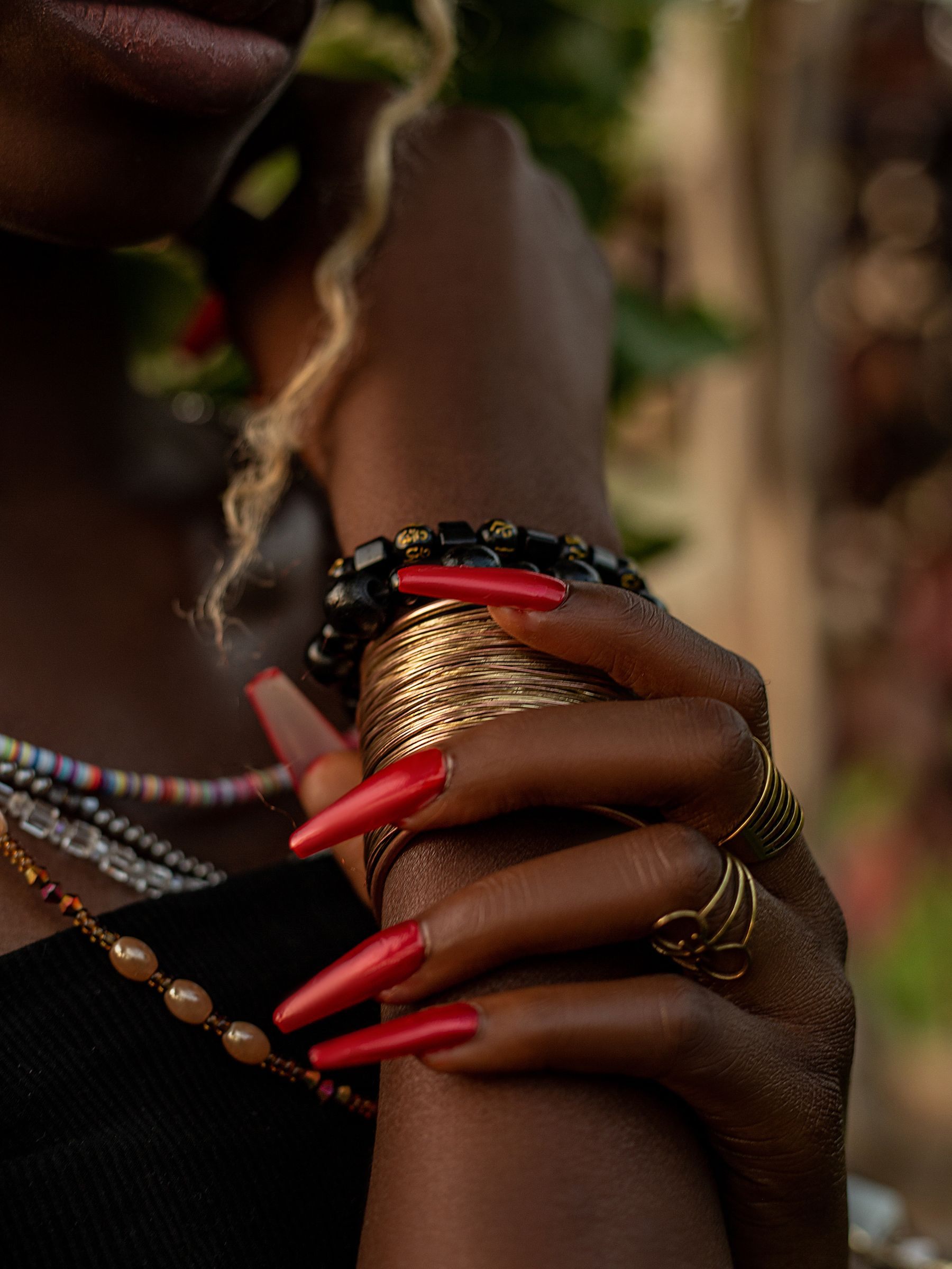 Long red nail extensions on a hand stacked with gold bangles and rings