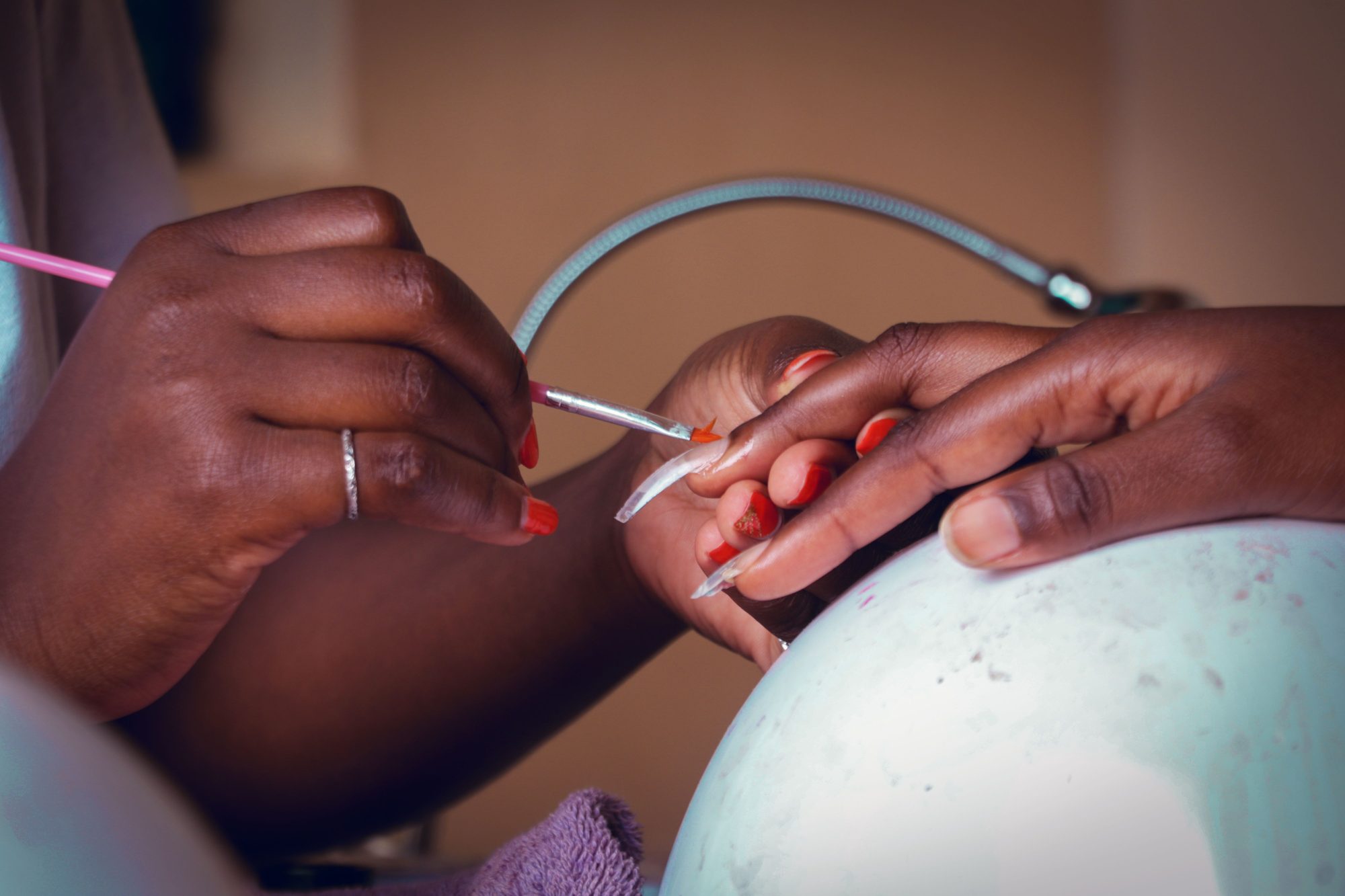 A nail technician painting fine detail onto a long nail extension