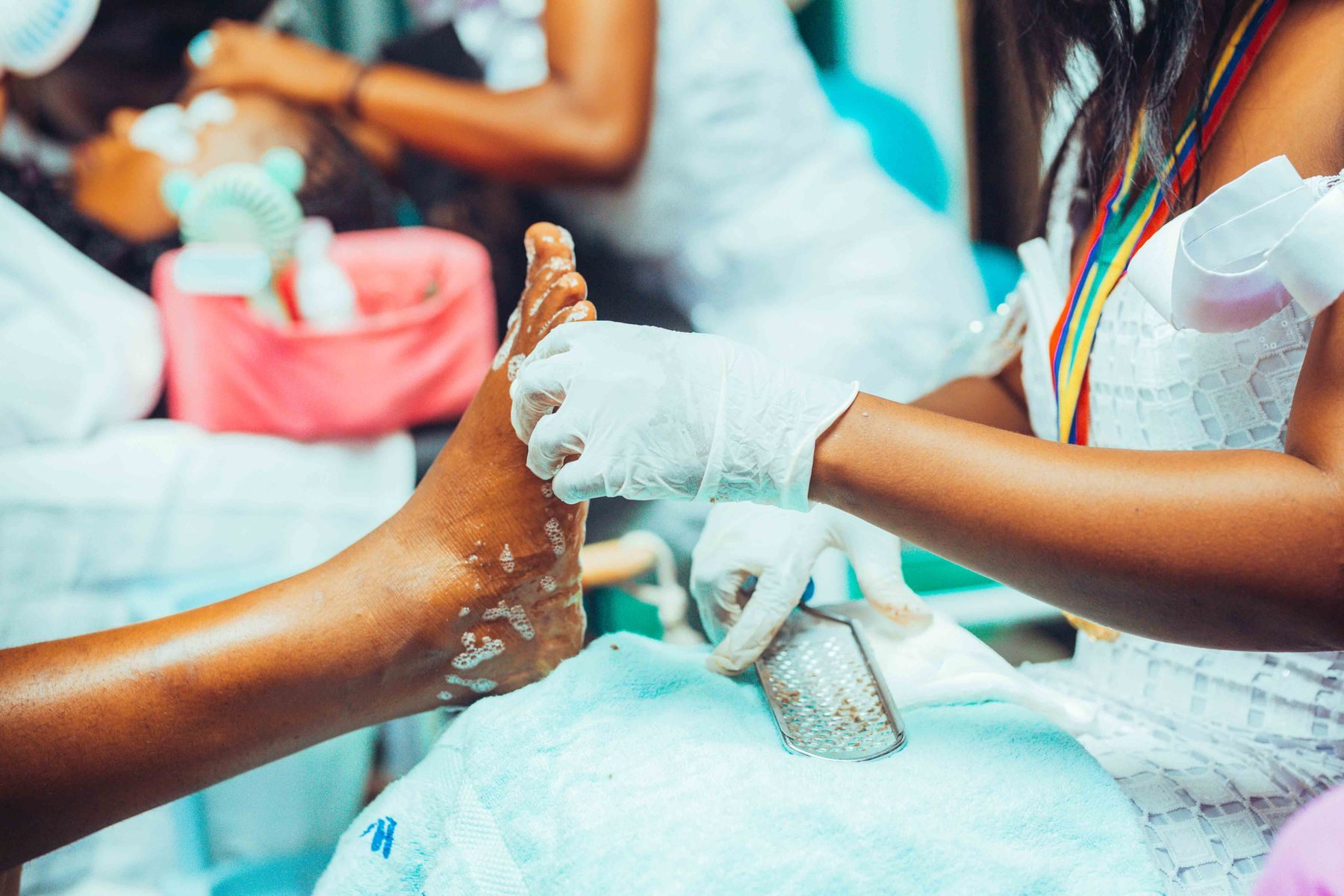 A technician in gloves smoothing a client’s foot during a pedicure