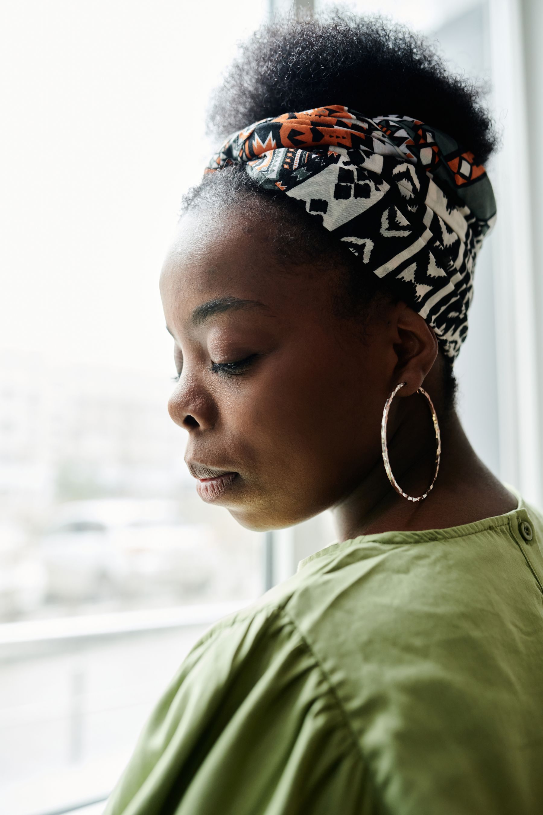 Natural hair worn up with a patterned headwrap, by a bright window